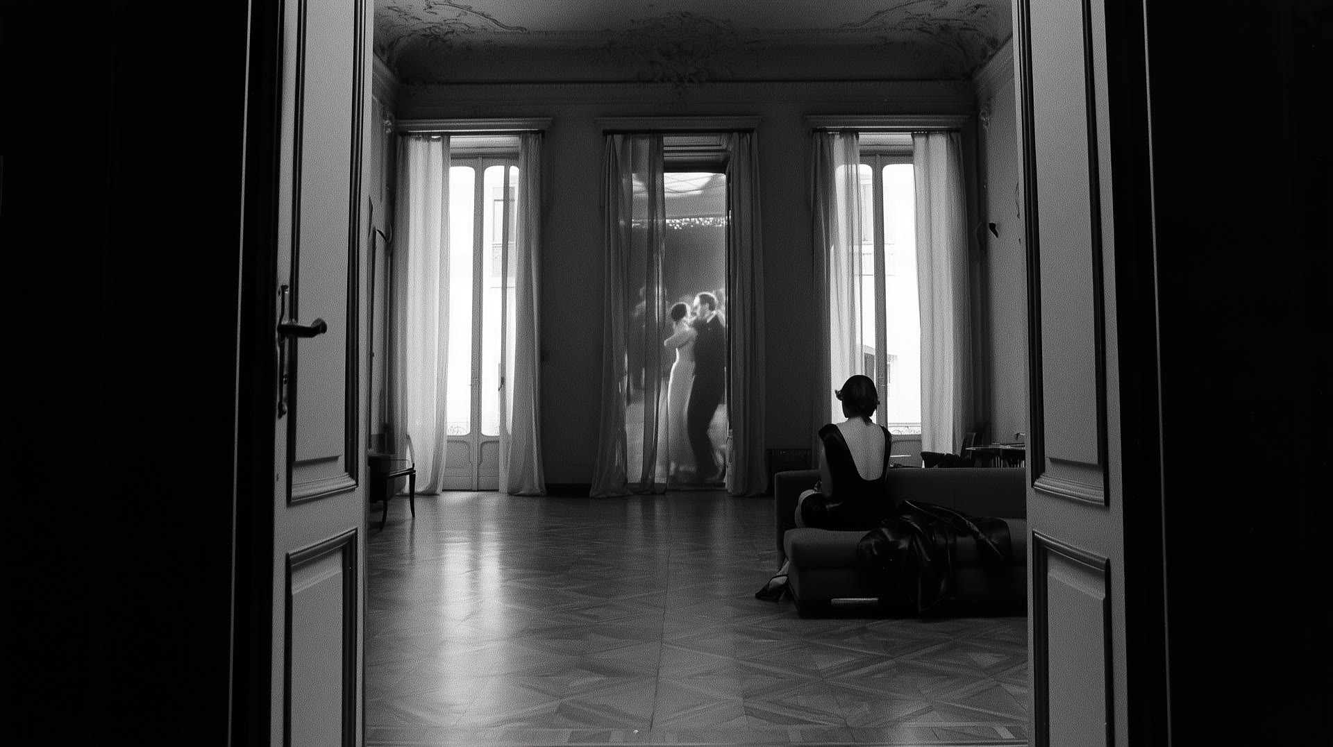 A woman in black seen from behind, watching a couple dance in a glowing doorway
